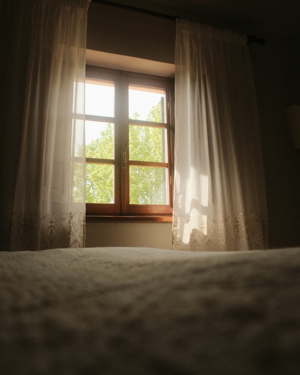 A bedroom with warm evening light coming through a window and sheer curtains